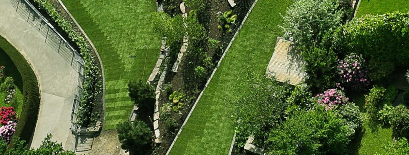 Blick von oben auf einen Park ähnlich angelegten Garten mit geschwungenen Rasenflächen und Beeten