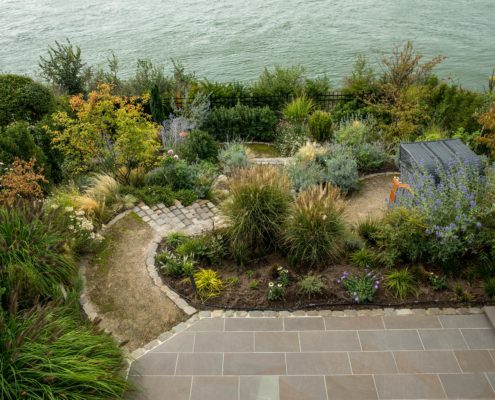 Blick auf eine Gartenanlage an einem See gelegen, mit einer Naturstein-Terrasse
