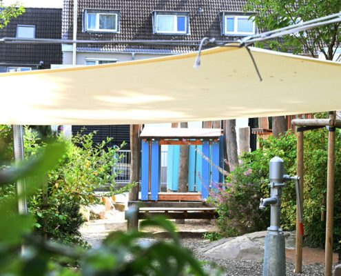 Blick auf das Kita-Gebäude mit Sonnensegel im Vordergrund
