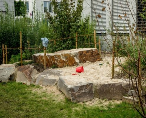 Große Natursteine bilden den Rahmen eines Sandbereichs