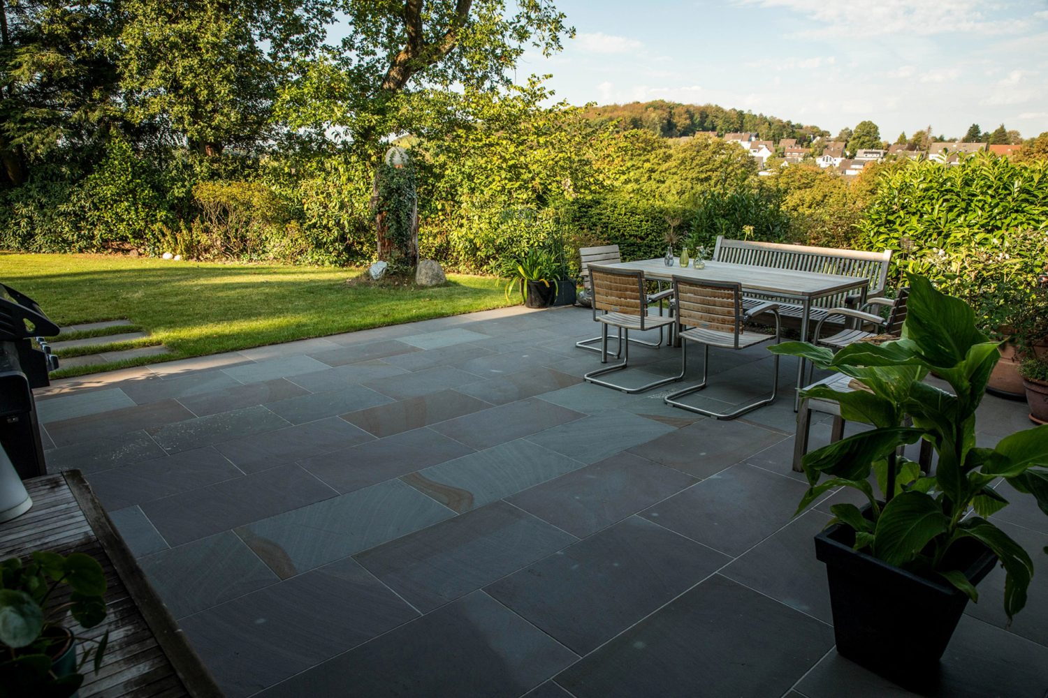 Großzügige Terrasse aus Grauwacke mit Sitzgelegenheit neben Beeten und Rasen