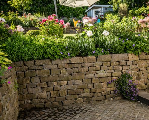 Natursteinmauer und blühendes Gartenbeet